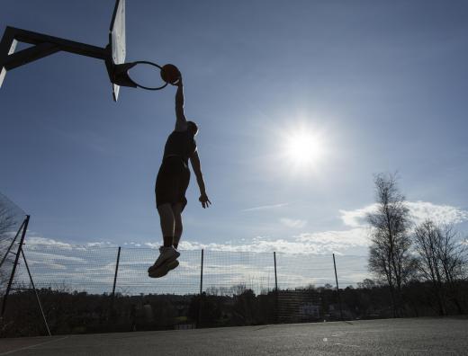 During a jump shot, a basketball player leaps up and drops the ball into the hoop.
