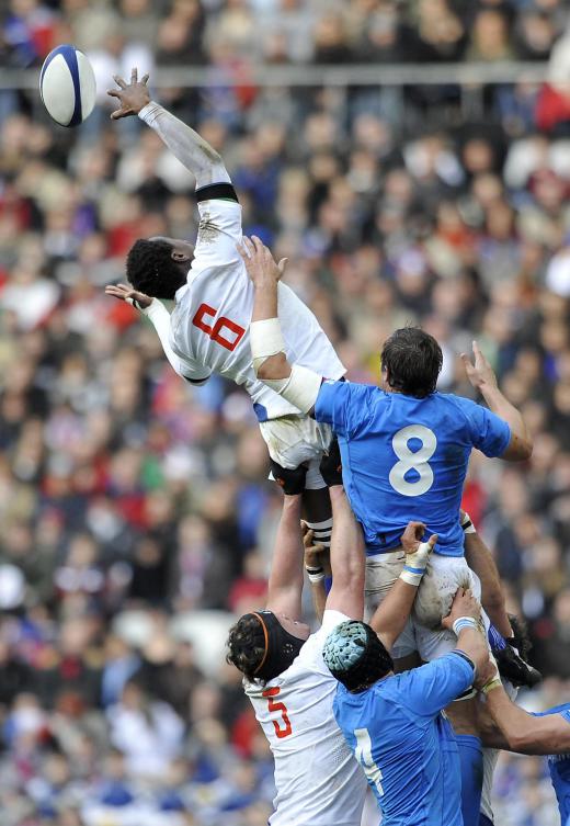 Rugby player being lifted up by his teammates to catch the ball.